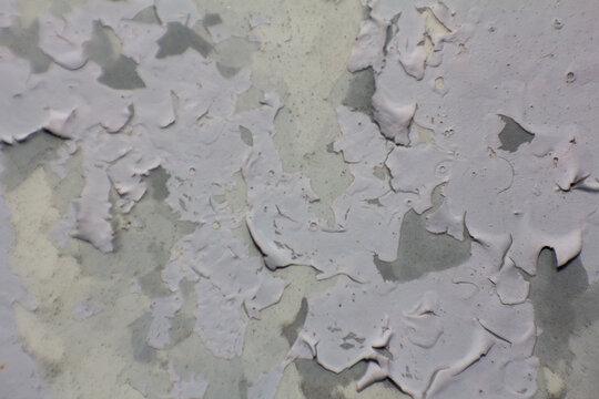 Close-up of peeling paint on an old weathered surface, showing textured layers of chipping grey and white paint creating an abstract background for design