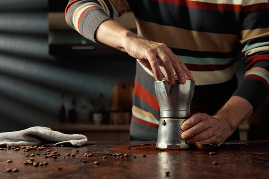 A man in a striped jumper is about to make coffee in an old Italian coffee maker.