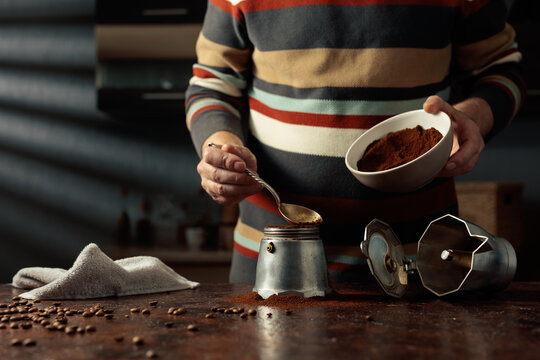 A man in a striped jumper is about to make coffee in an old Italian coffee maker.