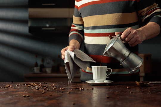 A man in a striped sweater is poured coffee from a geyser coffee maker into a white cup.