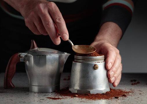 Man  is poured grounded coffee into a classic Italian aluminium moka pot.