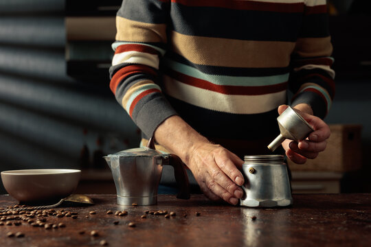 A man in a striped jumper is about to make coffee in an old Italian coffee maker.