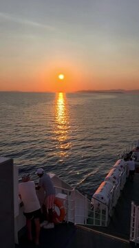 Supetar, Croatia - August 03, 2026: Sunset over calm sea viewed from a ferry with passengers observing the horizon and reflections on the water creating a serene atmosphere