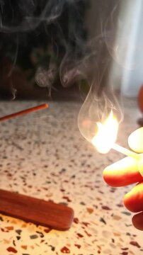 A hand striking a match against a matchbox in a dark room
