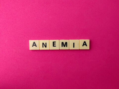 Plastic letter tiles arrangement spelling out the medical condition ANEMIA on a solid bright pink background