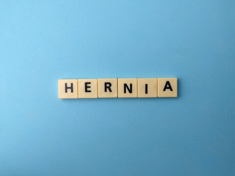 Plastic letter tiles centered on a solid light blue background spell out the medical term HERNIA