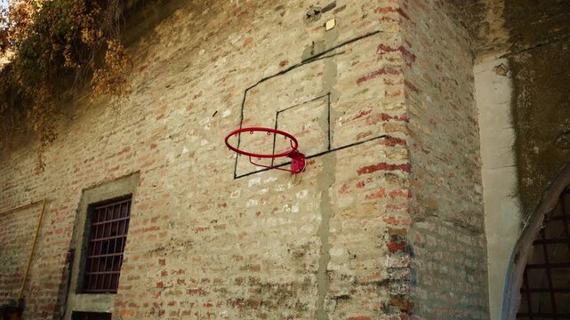 Improvised basketball hoop attached to a historic brick fortress wall. Concept of streetball culture, urban sports, makeshift playgrounds, local community recreation, and gritty sports aesthetics. 4K.