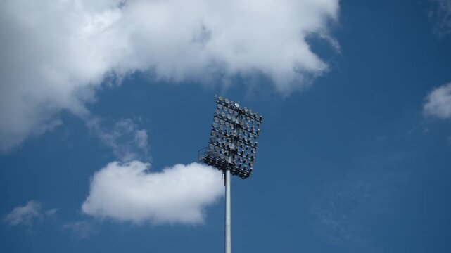 Stadium floodlight mast silhouetted against a cloudy blue sky. Concept of sports infrastructure, arena illumination, game preparation, and outdoor event facilities. 4K.