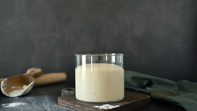 Сlose-up timelapse of natural wild yeast sourdough starter fermenting and growing inside a transparent glass jar.