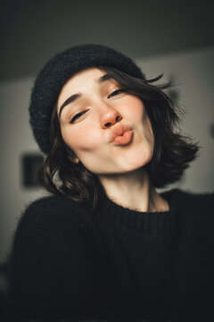 people of ai, modern girl doing kissy face, portrait, black knitted beanie and a playful kiss, photorealistic