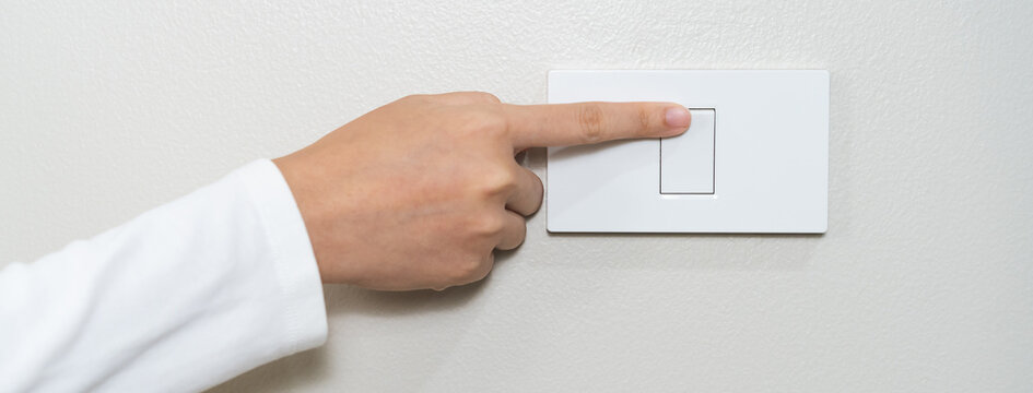 Asian young woman hand turn off on lighting switch at home room. Finger pushing light switch turn on or off white switch on wall for saving, control power electrical energy, eco environment concept.