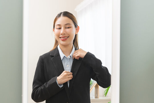 Get dress, pretty asian young woman, business woman standing wearing suit formal with shirt, female getting dressed preparing before go to work looking reflection in the mirror in the morning at home.