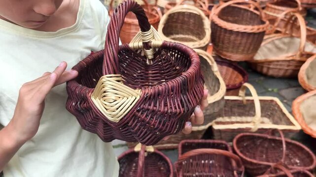 Child examines intricately woven wicker basket with a handle, surrounded by various other baskets in a vibrant market setting, showcasing craftsmanship and detail