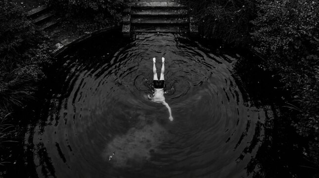 Overhead view of a person diving headfirst into dark water, creating ripples, with steps and trees in the background.