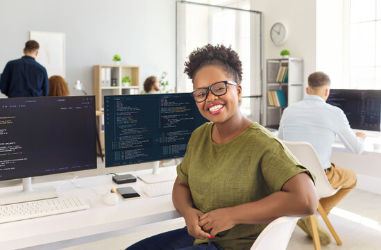 Developer woman programmer coding in modern office. Smiling IT specialist at a computer workstation with code on screens, perfect for tech and business. Team portrait, smiling and productive.