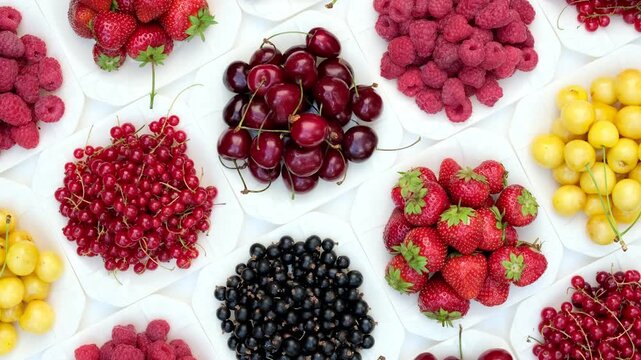 Rotating top view of assorted fresh summer berries including strawberries cherries raspberries and currants on white plates