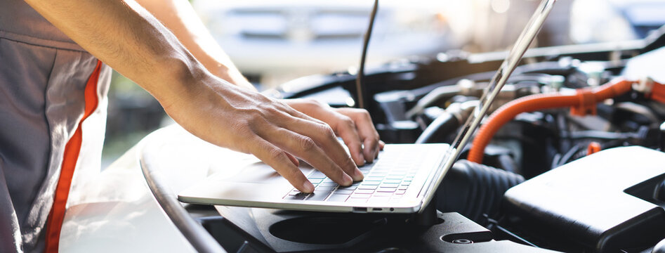 Professional car mechanic hands using laptop computer for diagnostic checking system and vehicle performance analysis during engine service maintenance in auto repair workshop garage.