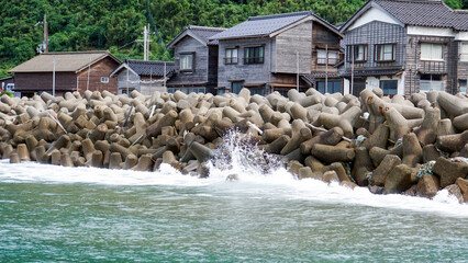 打ち寄せる波を防ぐテトラポットの護岸と山裾に広がる古い集落 © ToYoPHoTo