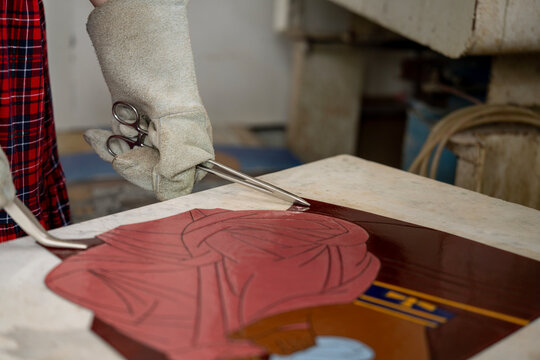 Artisan wearing a heat-resistant protective glove holding metal tools to adjust a hot cloisonne enamel artwork plate cooling on a marble slab in a workshop.