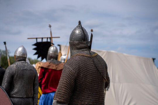 Medieval warriors wearing steel chainmail armor and pointed helmets seen from behind during a historical reenactment festival outdoors.