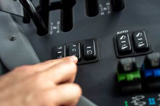 Driver pressing speed control switch on dashboard panel inside modern agricultural tractor cabin, adjusting cruise control and machinery settings during field work.