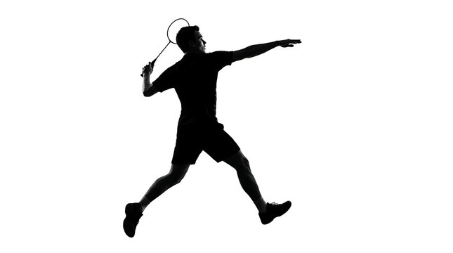 Man playing badminton during a jump smash with racket raised against a bright setting