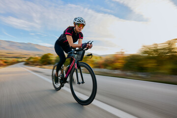 Naklejka premium Female Cyclist Riding Fast On Road Bike Through Countryside During Outdoor Training