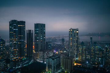Fototapeta premium Modern urban skyline at dusk with illuminated high-rise residential buildings under a moody evening sky, representing city life, architecture and urban development.