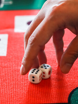 Close-up of a person's hand placing or rolling two white dice on a red and green gaming mat, capturing a moment of strategy and chance in a board game or casino play.