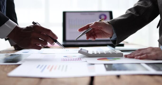Business professionals analyzing financial data using a calculator and laptop with charts, collaborating on a marketing strategy in an office workspace