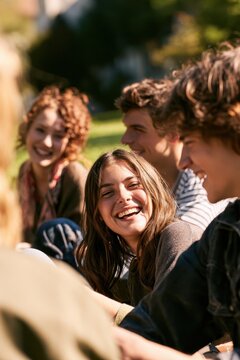 Diverse student friends sitting together outdoors, warm sunlight, joyful moment of friendship