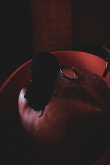 Rear view of a woman rinsing in a bathtub under warm dim lighting © Jef