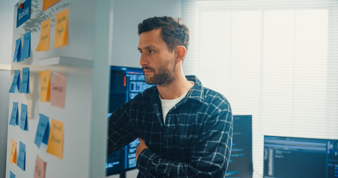 Young Caucasian male programmer write creative plan on whiteboard and coding on computer in home office workspace. AI technology, cybersecurity network, agile strategy, business innovation concept.