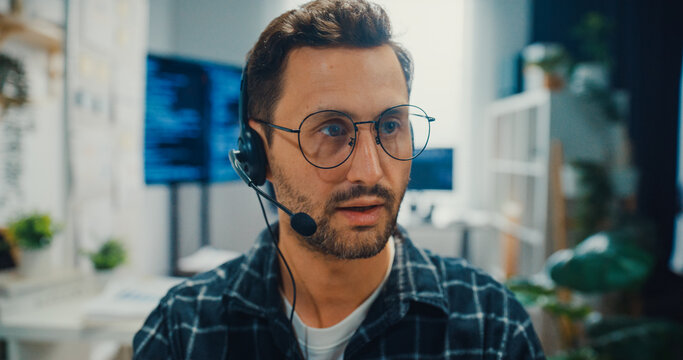Young Caucasian male technical support specialist wearing headset speaks on computer at office. Professional call center help desk, Cyber security operator service, Online client consultation concept.