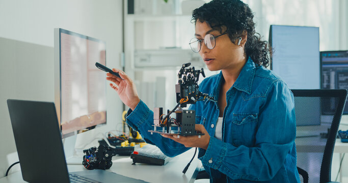 Young African American female robotics engineer discussing mechanical part on video call in laboratory. Remote work, virtual training, online meeting, future technology, technical support concept.