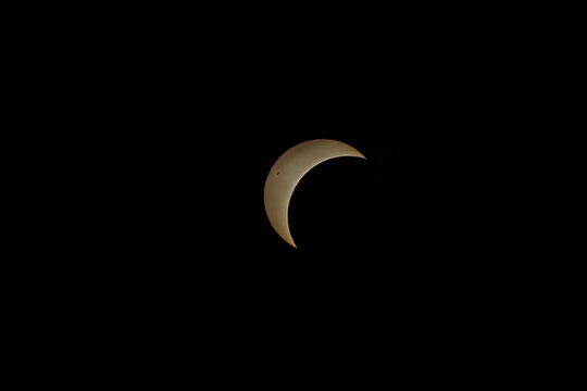 Partial solar eclipse showing a bright golden crescent in black sky