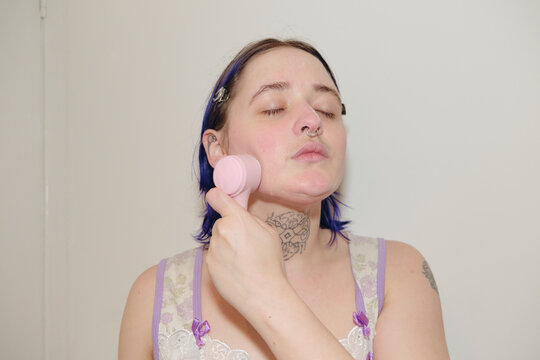 Non-binary person using a face cleansing brush