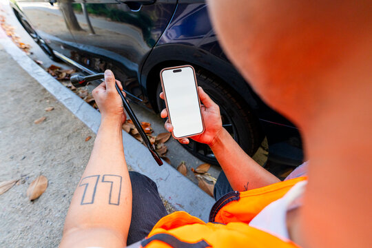 anonymous man using mobile phone roadside by car tire
