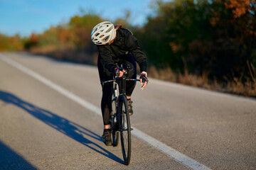 Naklejka premium Female Cyclist Sprinting on Empty Country Road During Autumn Training Ride at Sunset