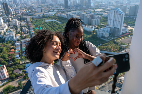 Two women take a joyful selfie over a cityscape.