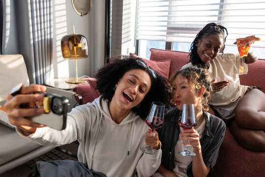 Three friends take a selfie enjoying wine and pizza.
