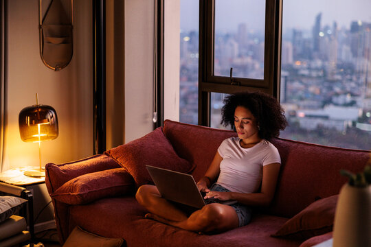 Woman Using Laptop on Sofa in Apartment at Dusk