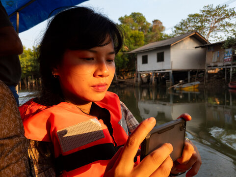Young woman taking pictures with a smartphone on a boat at sunset