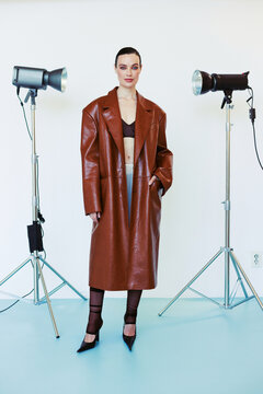 A woman in a chocolate leather coat standing on a studio setting.