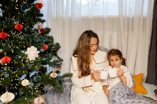 Happy mother and daughter drinking cocoa under the Christmas tree 