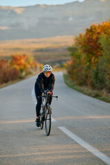 Naklejka premium Female Road Cyclist Training On Open Country Road At Sunrise With Autumn Scenery And Focused Pace