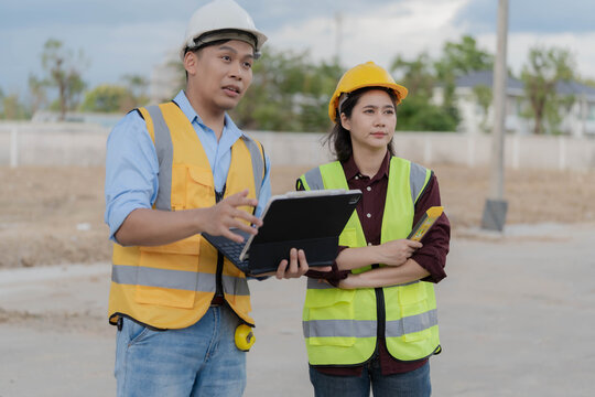 Asian male engineer holding tablet and pointing at construction site during inspection with colleague