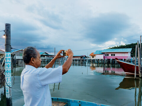 Elderly man taking a picture of waterfront houses by the lake