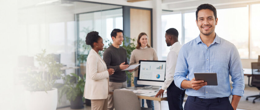 Businessman holding tablet with team in office stands smiling while diverse colleagues analyze data on computer screen in modern bright workspace for corporate business banner