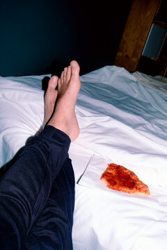 the bare feet of a man lead toward a slice of pizza on a bed